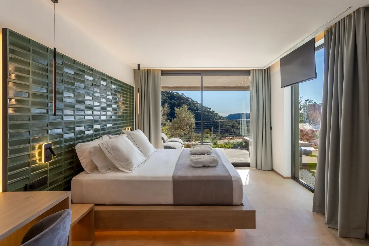 Habitación con cama grande vestida de blanco y gris, cabecero de azulejos verdes, escritorio de madera, cortinas