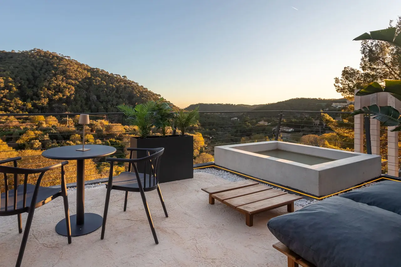 Piscina privada rectangular de agua clara en una terraza exterior con suelo de piedra, rodeada de vegetación, con mesa