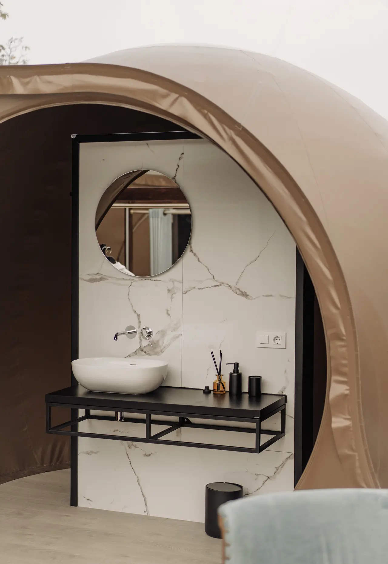 Interior de un baño con paredes de mármol blanco y negro, un lavabo blanco sobre un mueble negro, un espejo redondo