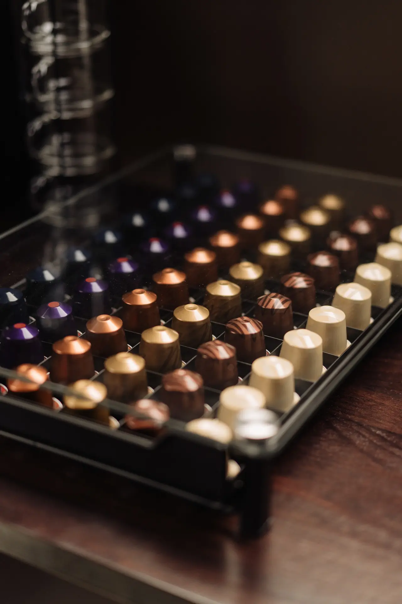 Caja organizadora negra con cápsulas de café de diversos colores y diseños ordenadas en filas, colocada