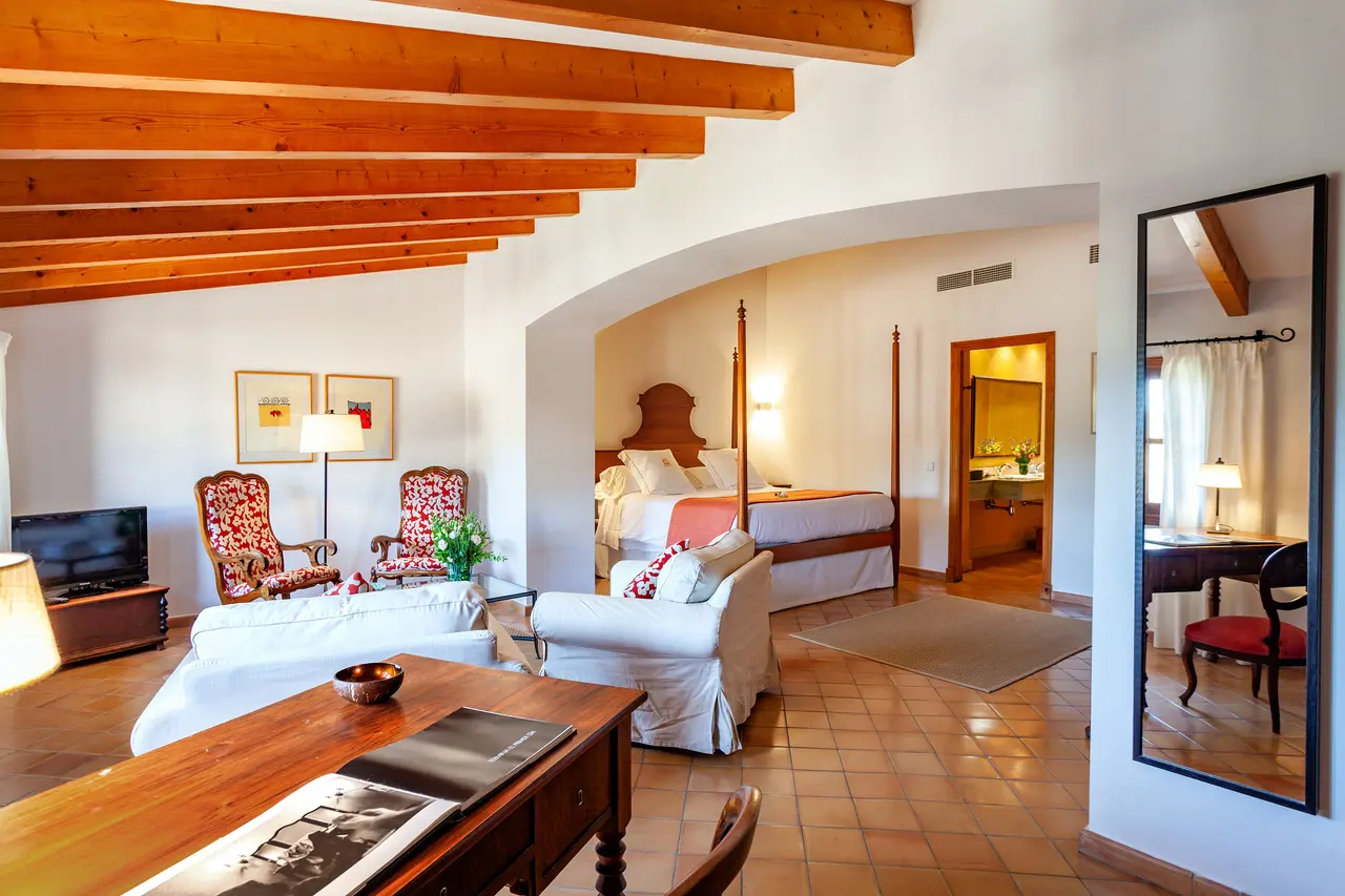 Vista de una junior suite con techos altos de vigas de madera, zona de estar con sofás blancos y sillones, cama