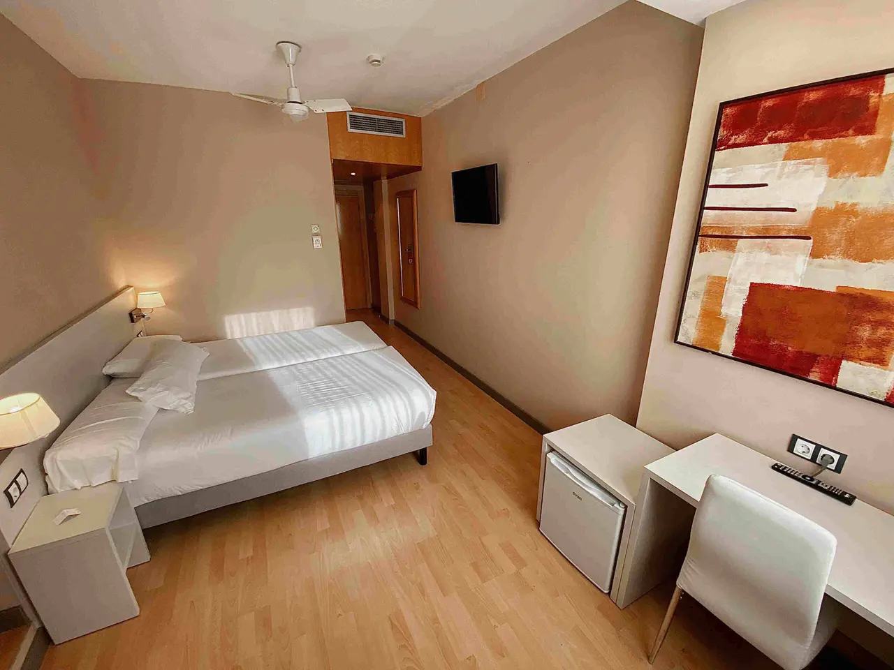Vista de una habitación de hotel con dos camas individuales juntas, mesitas de noche con lámparas, escritorio