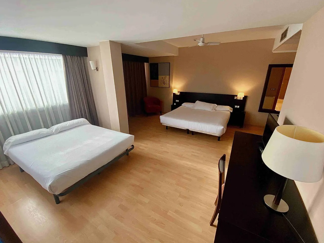 Vista general de una habitación de hotel con dos camas individuales separadas, suelo de madera clara, escritorio