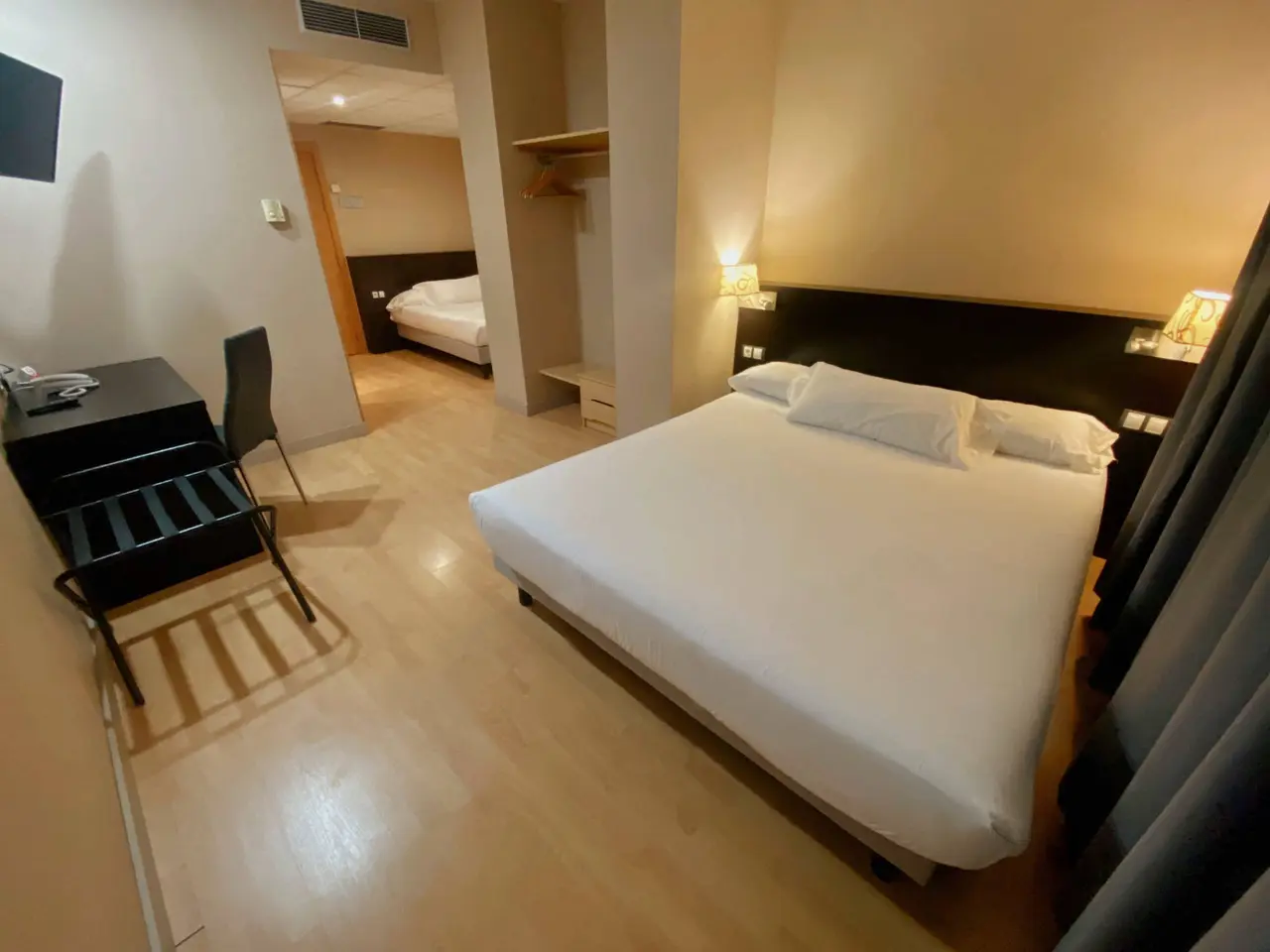 Habitación de hotel con cama doble grande vestida de blanco, cabecero oscuro, mesitas de noche con lámparas