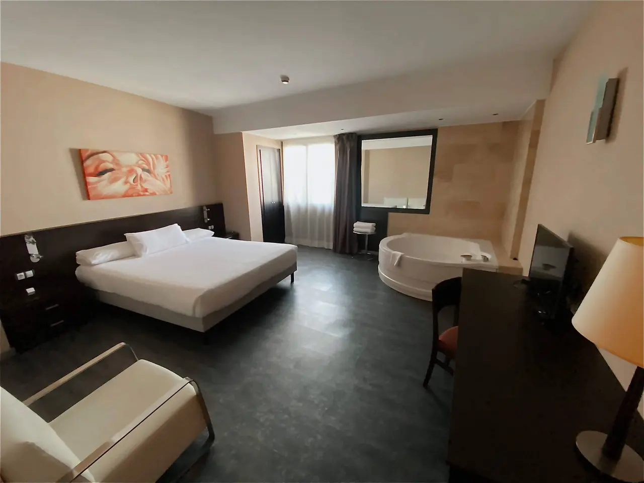 Vista general de una habitación de hotel con cama doble, jacuzzi circular en la zona de estar, escritorio con silla