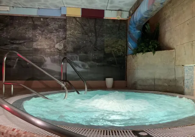Jacuzzi circular con agua burbujeante de color turquesa, rodeado de barandillas metálicas.