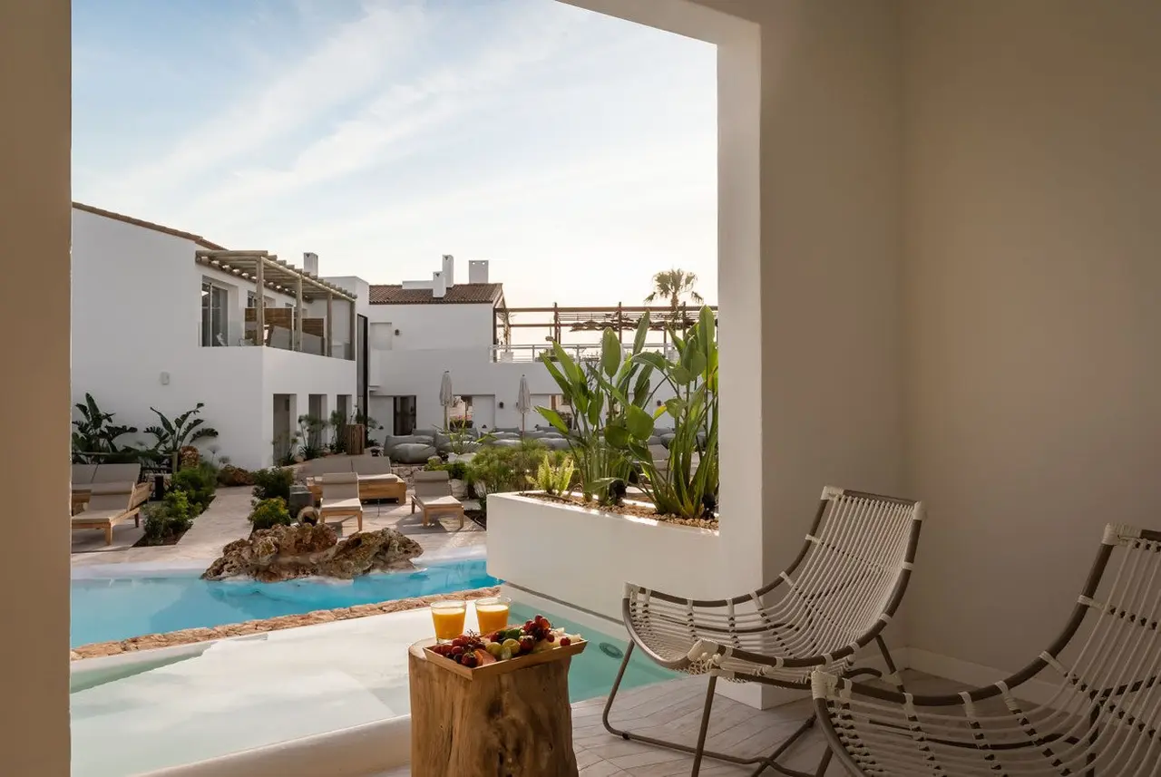 Vista desde el interior de una suite hacia una piscina privada en un patio con tumbonas y vegetación, rodeada