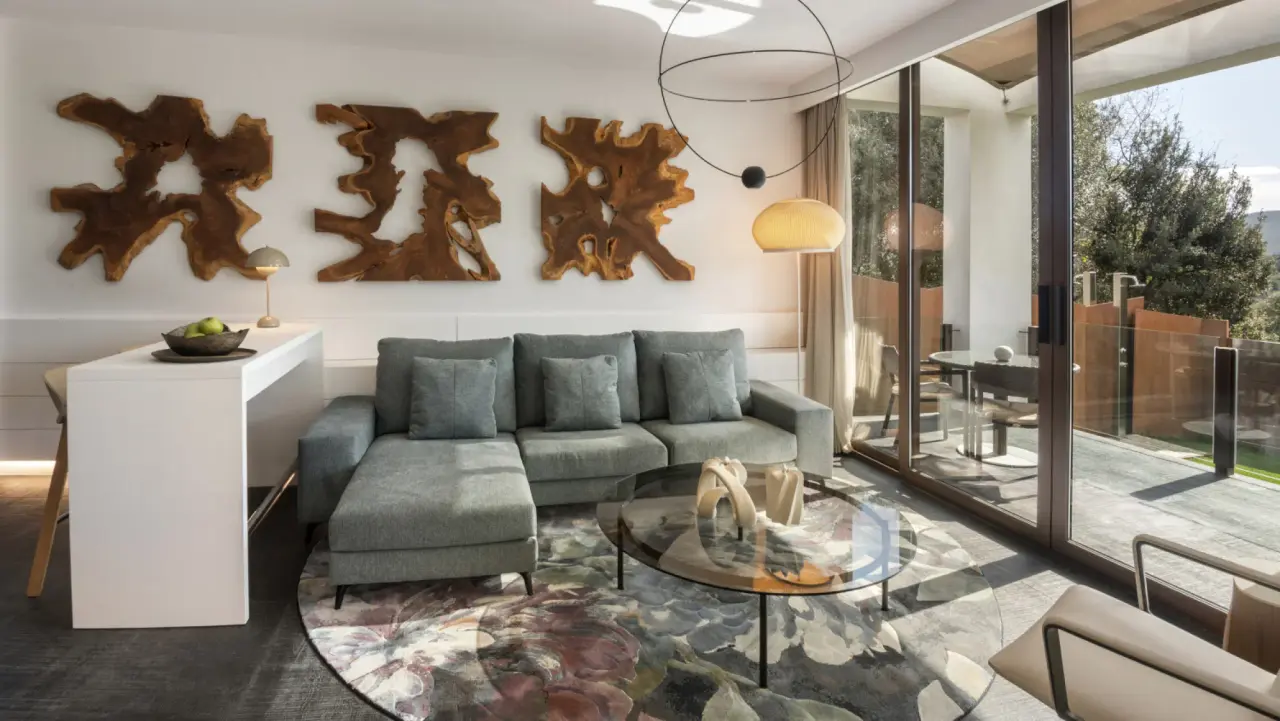 Sala de estar con sofá gris, mesa de centro redonda, obras de arte en madera en la pared y puertas de vidrio