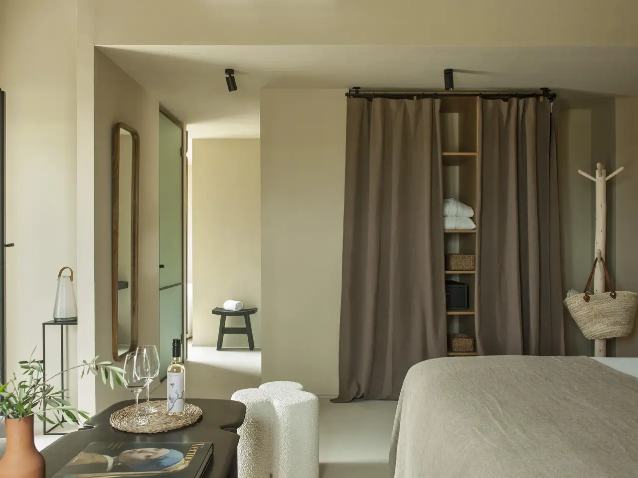 Interior de una suite con cama grande, mesa con bandeja de bienvenida, cortinas que separan una zona de vestidor