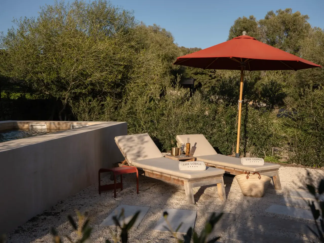 Vista de una piscina privada rectangular con borde de hormigón, dos tumbonas de madera con cojines beige
