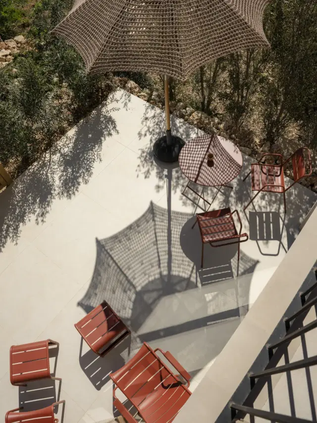 Vista aérea de una terraza exterior con suelo de baldosas claras, mesa redonda con mantel de cuadros, sillas plegables