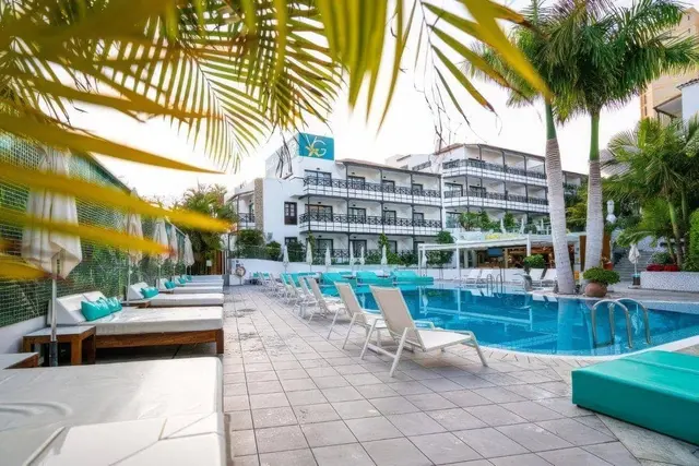Vista de la piscina rectangular del hotel con tumbonas blancas y turquesas alineadas en el borde, palmeras