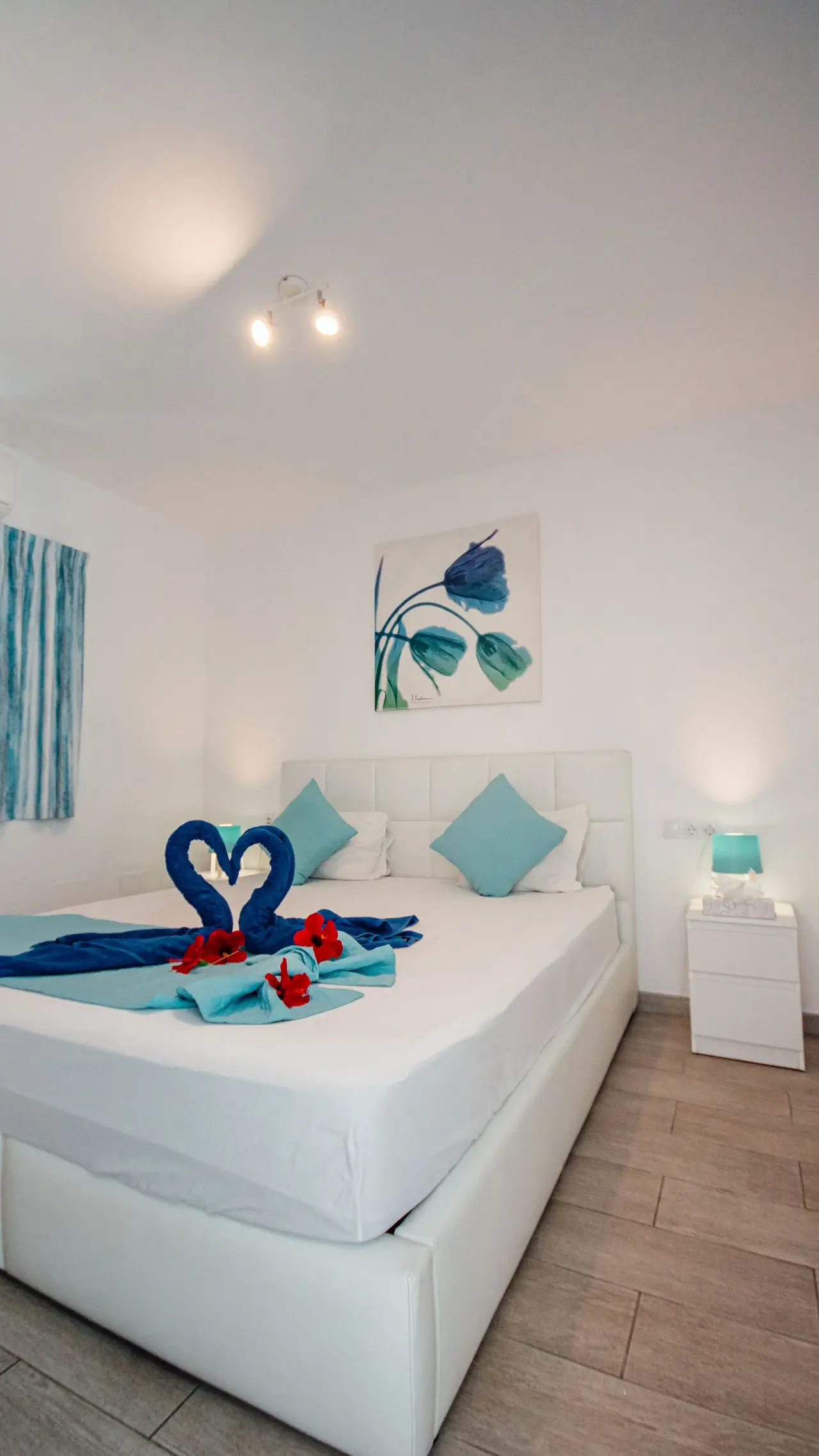 Habitación de bungalow con cama doble grande vestida de blanco, toallas azules dobladas en forma de cisnes