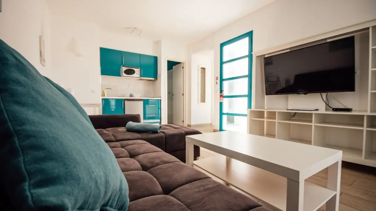 Interior de un bungalow con sala de estar, sofá marrón grande, mesa de centro blanca, televisor montado en la pared