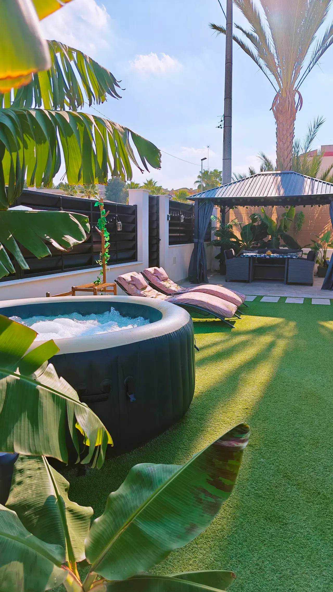 Jacuzzi hinchable exterior en un jardín privado con césped artificial, rodeado de plantas tropicales como plataneras