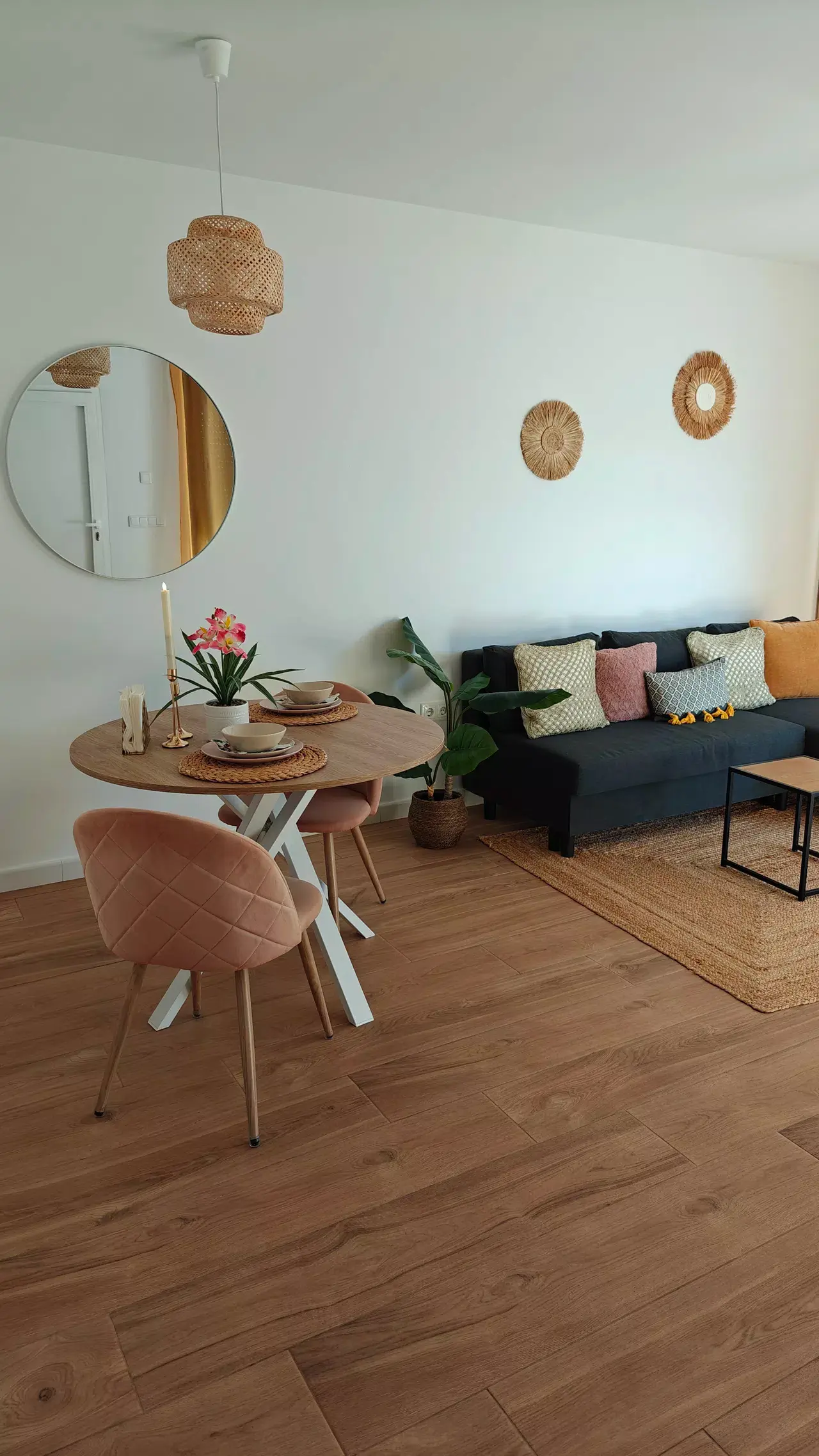 Interior de un salón comedor con suelo de madera clara, mesa redonda de comedor con sillas tapizadas en rosa, sofá