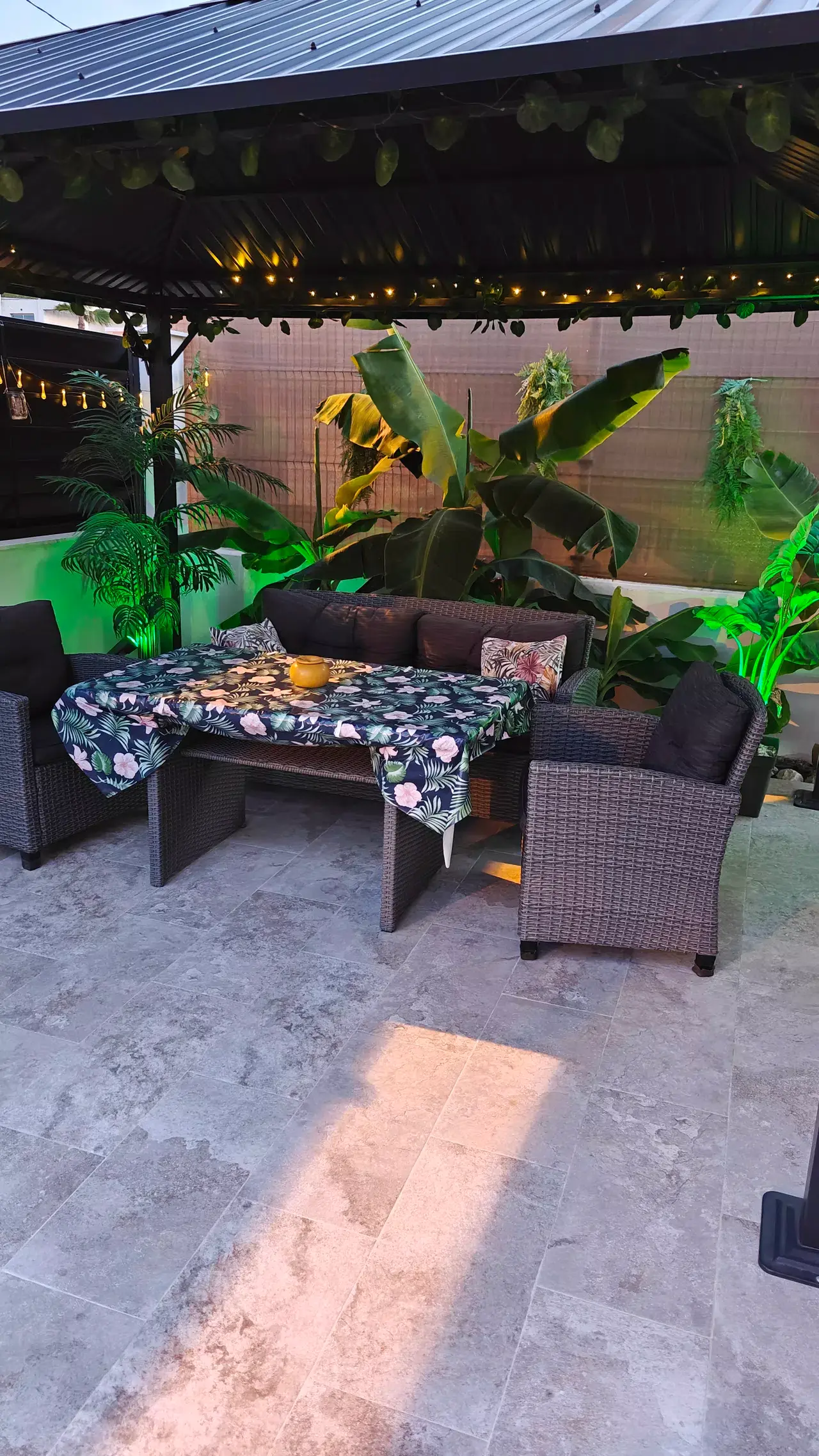 Terraza exterior con suelo de baldosas de piedra, bajo un techo de estructura metálica con luces decorativas.