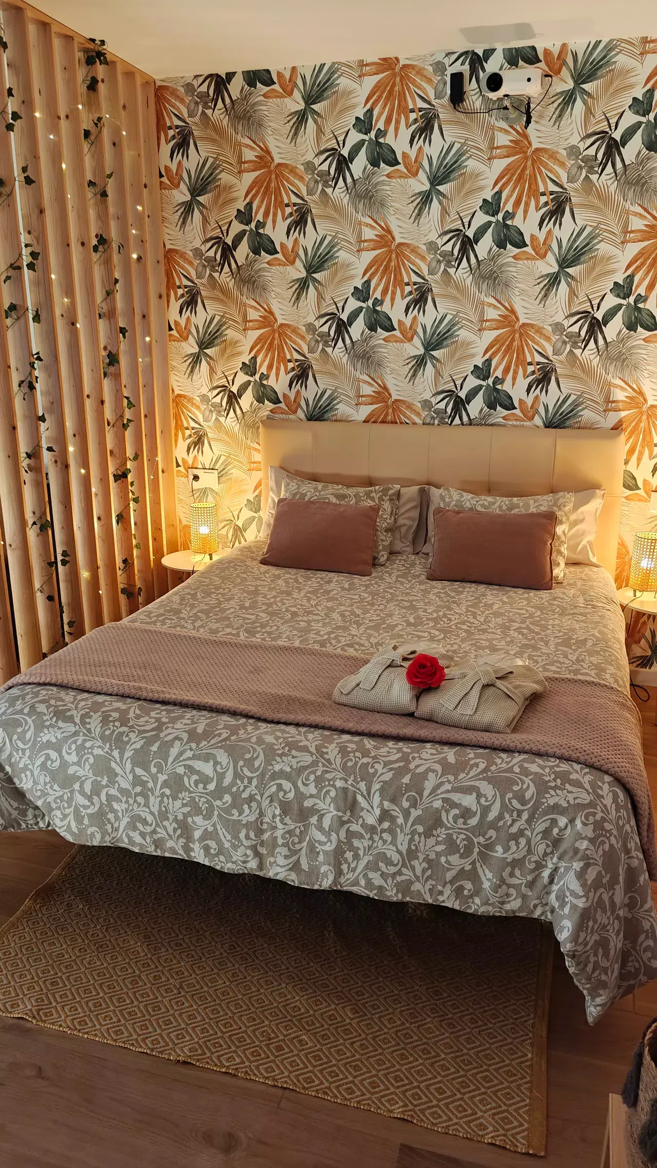 Habitación con cama doble grande vestida con colcha de estampado floral en tonos beige y blanco, dos almohadas