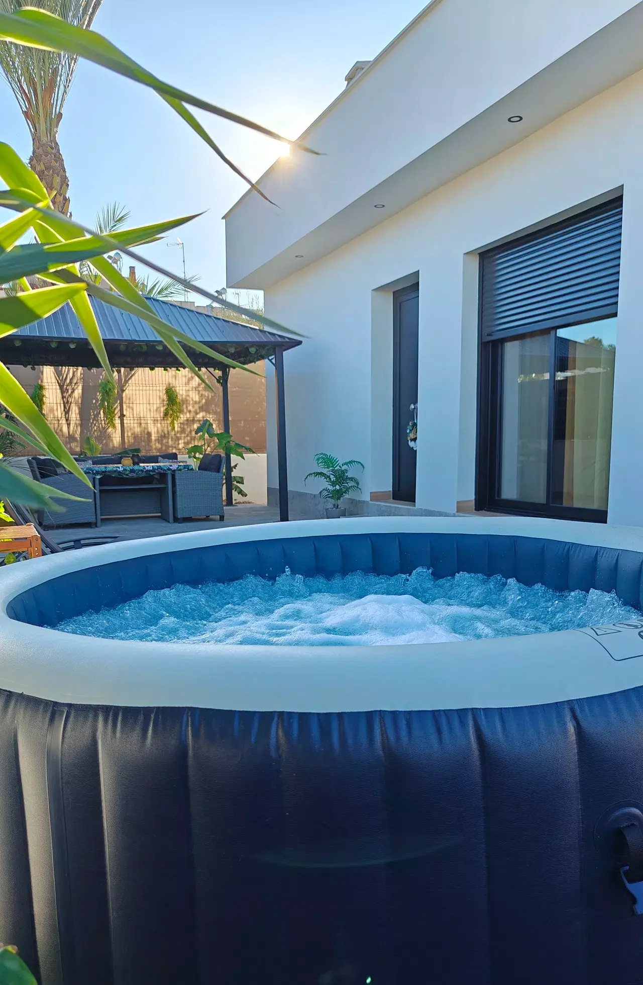 Jacuzzi hinchable exterior con agua burbujeante en un jardín privado junto a una villa blanca moderna.