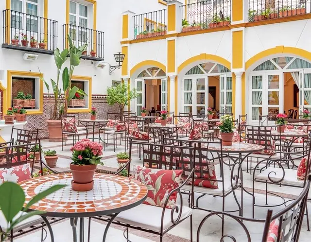 Patio interior de un edificio andaluz con paredes blancas y detalles amarillos, balcones con barandillas negras