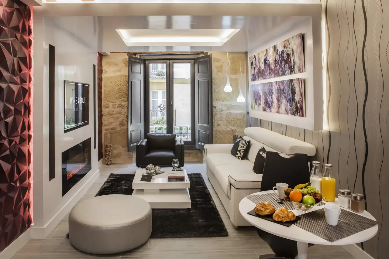 Vista de una sala de estar en una suite con sofá blanco, sillón negro, mesa de centro, chimenea eléctrica, mesa