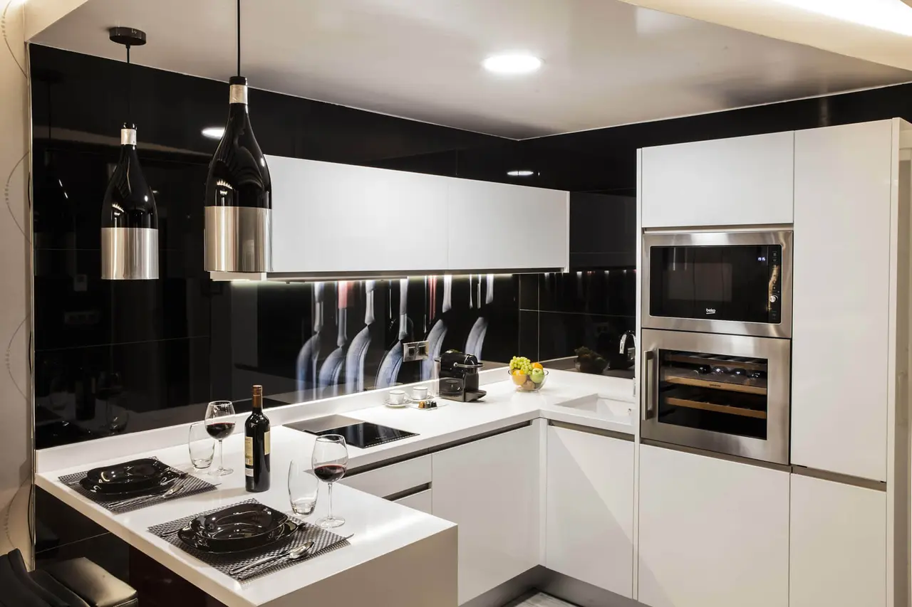 Cocina moderna con isla central blanca, encimera negra, electrodomésticos de acero inoxidable, dos lámparas colgantes
