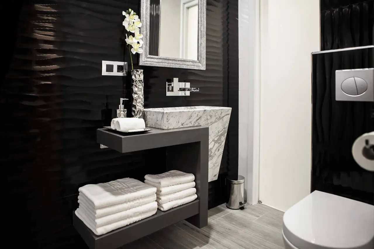 Baño moderno con paredes negras texturizadas, lavabo de piedra rectangular sobre un mueble flotante gris, espejo