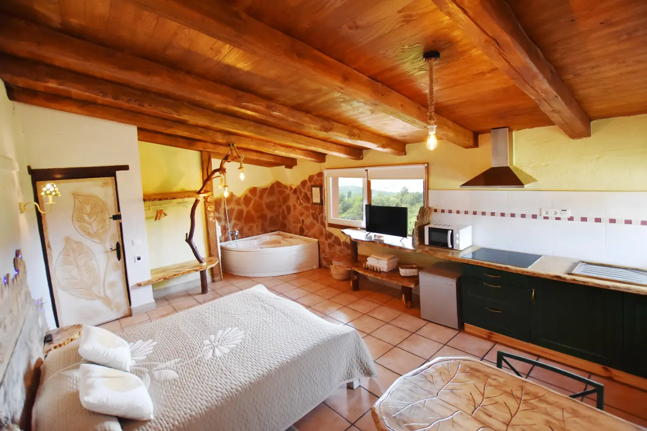 Habitación rústica con techo de vigas de madera, cama grande, cocina equipada y bañera de hidromasaje