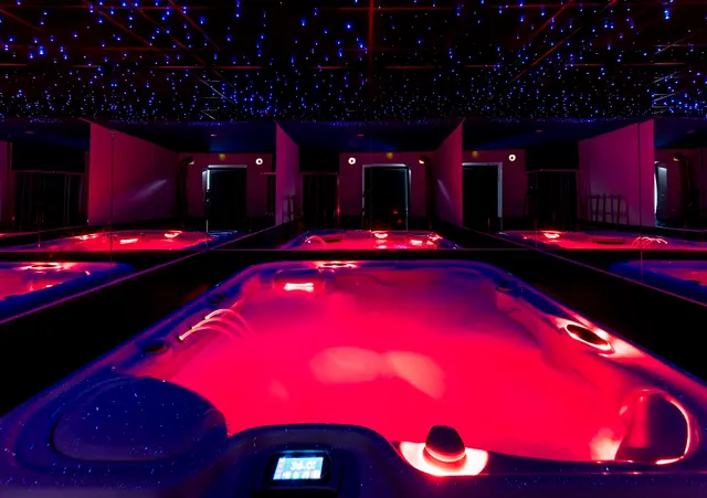 Jacuzzi privado iluminado en rojo bajo un techo estrellado en una sala interior con varias unidades más.