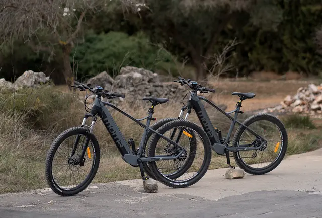 Dos bicicletas eléctricas aparcadas en un camino rural rodeado de vegetación y rocas.