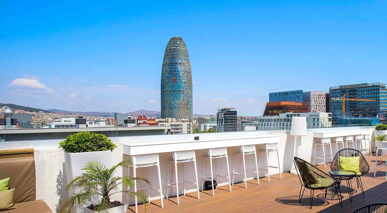 Vista desde una terraza con bar y mobiliario exterior hacia la Torre Glòries y el skyline de Barcelona bajo un cielo