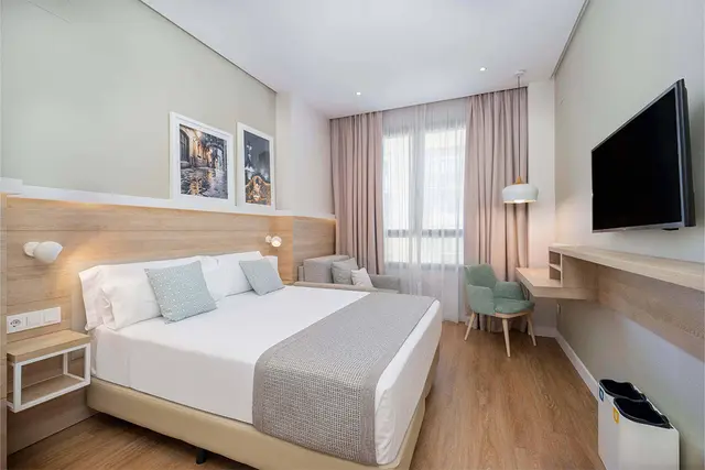 Vista de una suite de hotel con cama doble grande con cabecero de madera, dos cuadros decorativos, escritorio